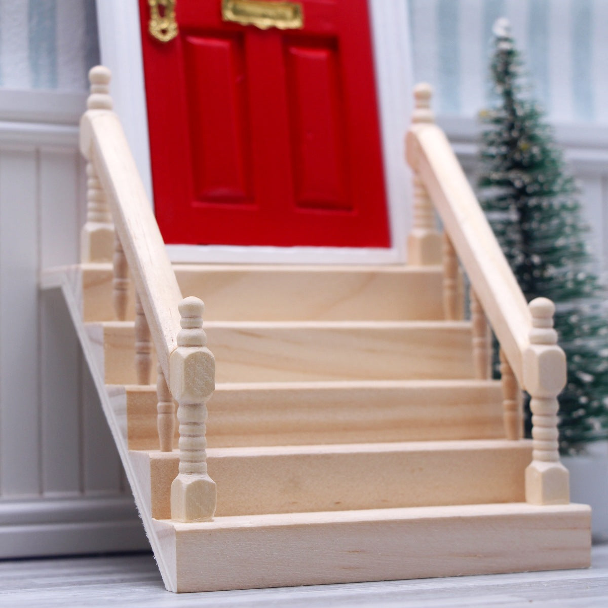 Wooden staircase model in front of a red door with a Christmas tree in the background